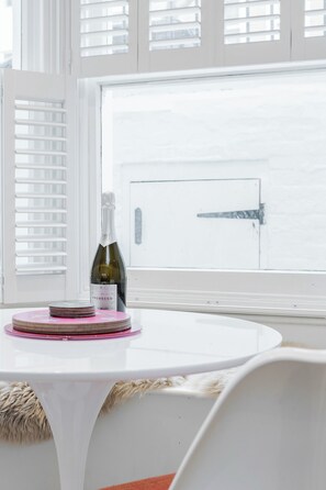 A white table with a bottle of wine and coasters, a window with blinds, and a door in the background. - Stylish Chelsea Apartment | 2 Bedrooms | Patio Living (London)