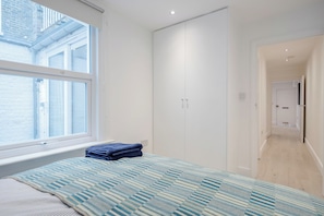 Quarto com uma janela grande, cama com colcha estampada e um guarda-roupa.