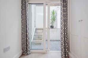 A room with a sliding glass door leading to a small outdoor area with a staircase and a potted plant. - Stylish Chelsea Apartment | 2 Bedrooms | Patio Living (London)