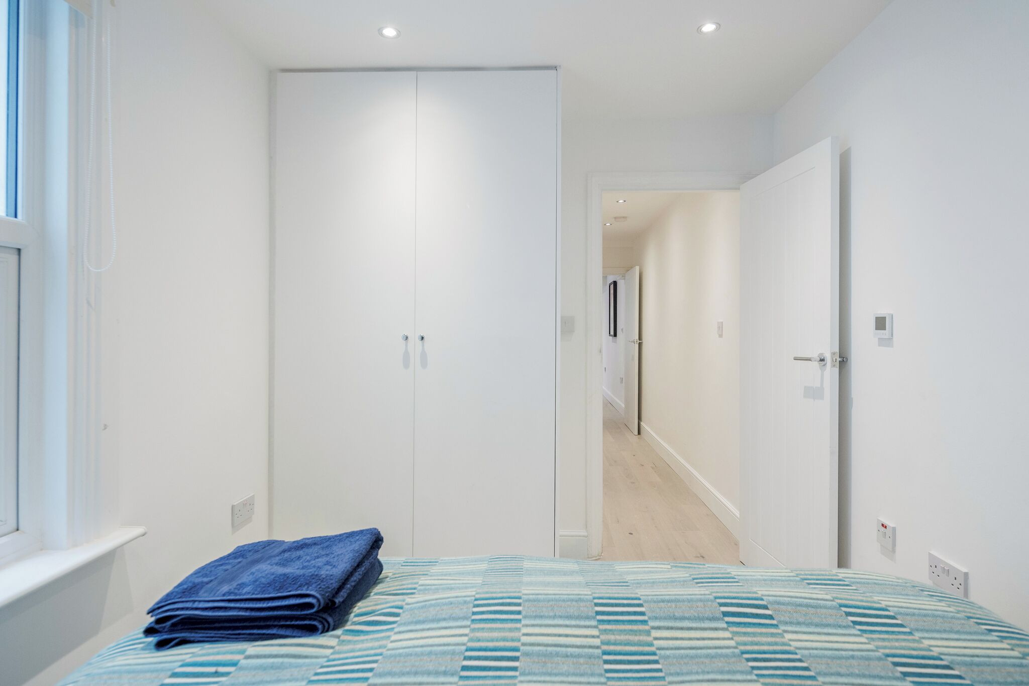 A bedroom with a bed, a wardrobe, and a hallway leading to another room.