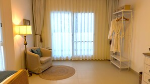A room with a sofa, a lamp, a round rug, a window with curtains, and a clothing rack.