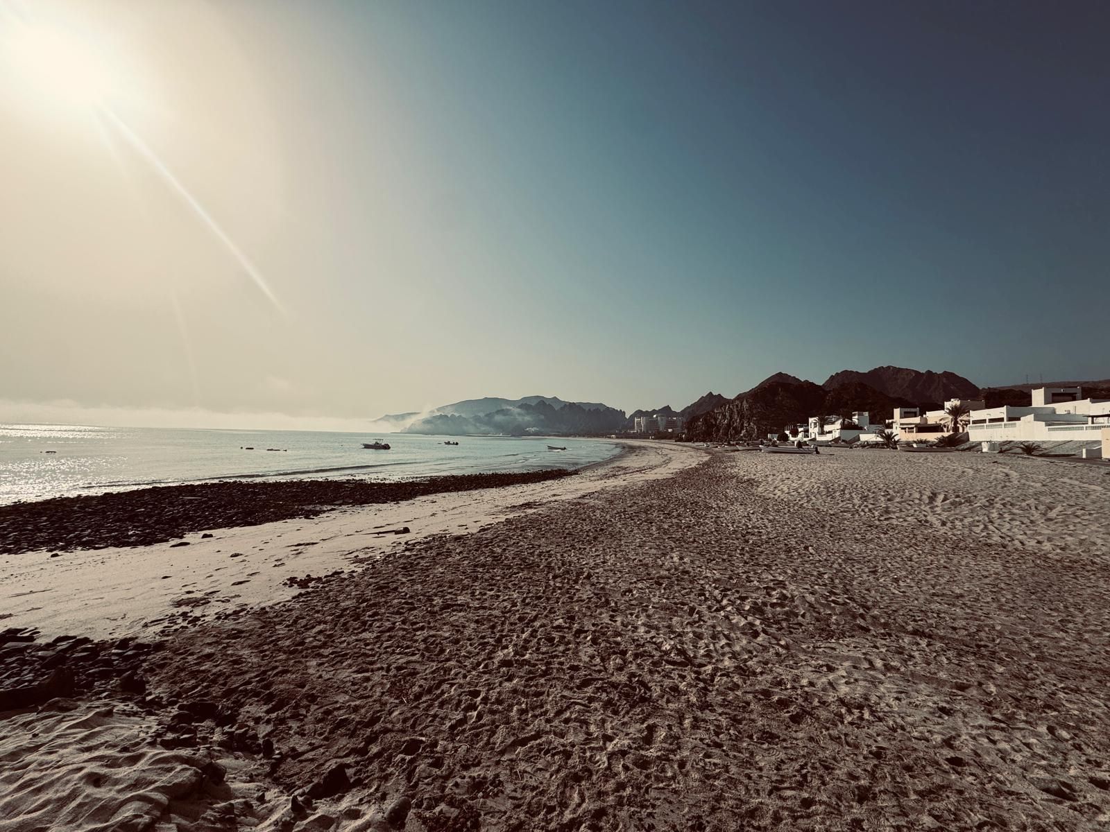 Een strand met een rotsachtige kustlijn, een heldere lucht en gebouwen op de achtergrond.