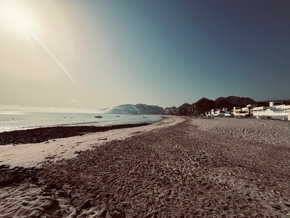 A beach with a rocky shoreline, a clear sky, and buildings in the background.