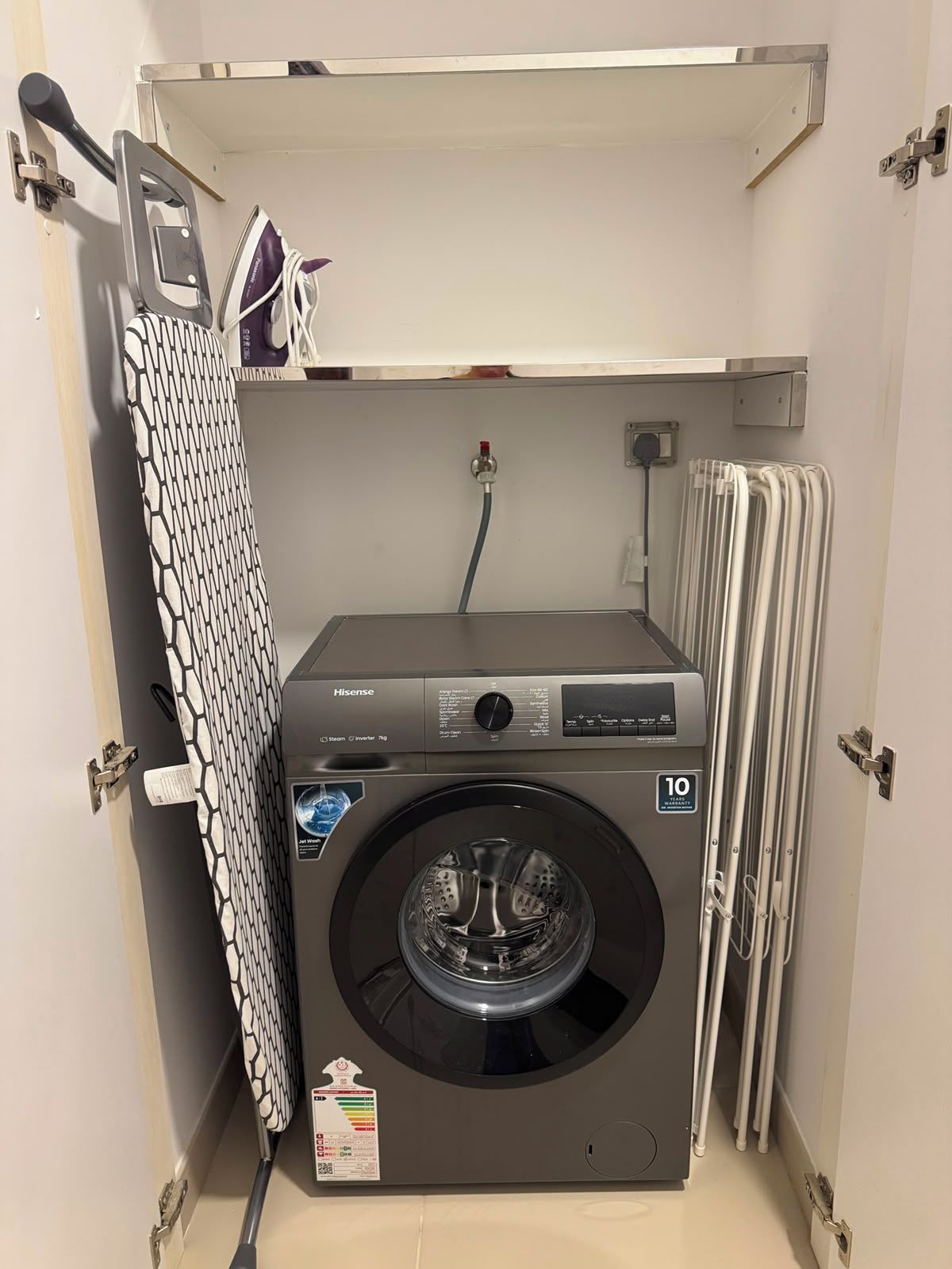 Een compacte, wandgemonteerde wasmachine met een bedieningspaneel, een slang en een label dat een garantie van 10 jaar aangeeft.