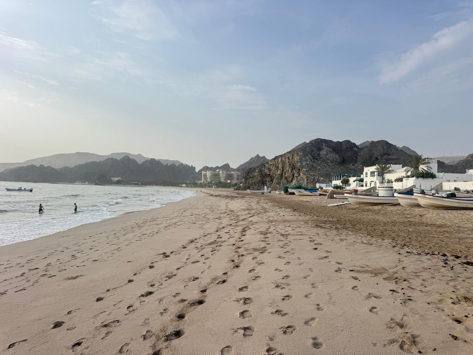 Ein Strand mit Fußspuren, Booten und Gebäuden im Hintergrund.