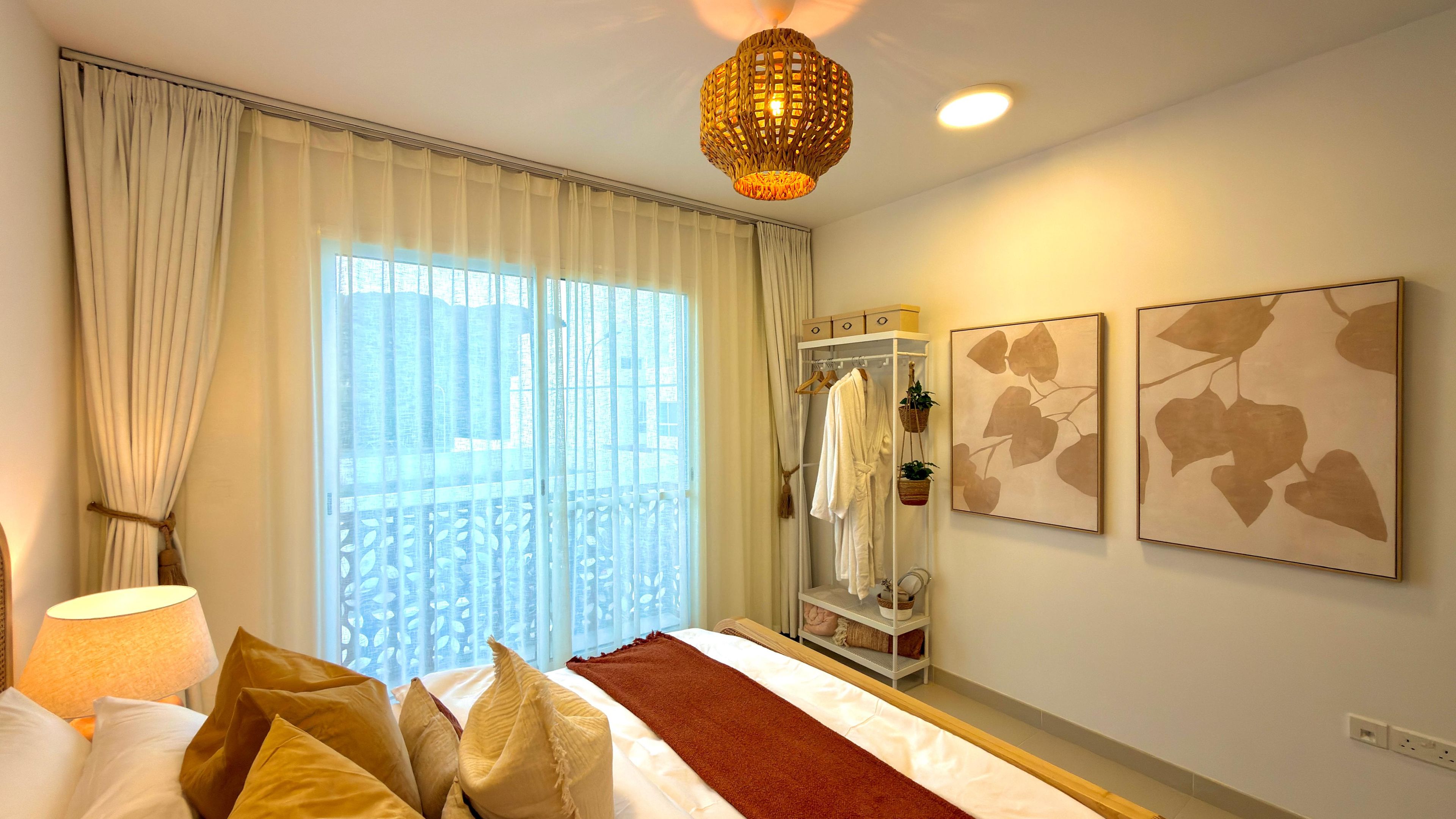 Hotelkamer met een bed, een raam met gordijnen, een hanglamp en twee aan de muur bevestigde kunstwerken.