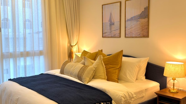 A hotel room with a bed, a nightstand with a lamp, and two paintings on the wall.