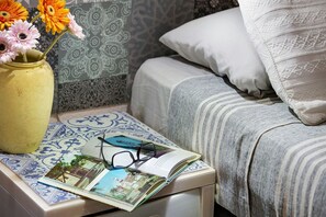 Ein Bett mit einer gestreiften Decke, einem Kopfkissen und einem Nachttisch mit einem Buch, einer Brille und einer Vase mit Blumen.
