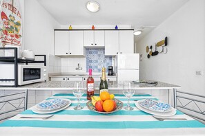 A modern kitchen with white cabinets, a microwave, a coffee machine, and a dining area with a striped tablecloth. - Quiet, comfortable apartment just 5 minutes from Yumbo (Maspalomas)