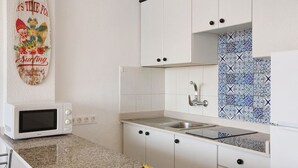 Una cucina con mobili bianchi, un forno a microonde, un lavello e uno schienale rivestito di piastrelle azzurre e bianche.