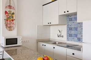A kitchen with white cabinets, a microwave, a sink, and a backsplash with blue and white tiles. - Quiet, comfortable apartment just 5 minutes from Yumbo (Maspalomas)