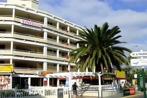 Ein mehrstöckiges Hotel mit Balkonen, einer Palme und einem Schild, das ein Restaurant anzeigt.