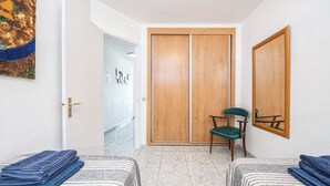 Una stanza con due letti, un'armadio in legno, una sedia e uno specchio fissato alla parete.