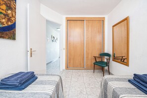 A room with two beds, a wooden wardrobe, a chair, and a wall-mounted mirror. - Quiet, comfortable apartment just 5 minutes from Yumbo (Maspalomas)