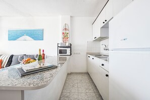 Une cuisine compacte équipée d’un four à micro-ondes, d’un grille-pain et d’un évier. On y trouve également un petit coin repas avec une table et des chaises, ainsi qu’un tableau représentant la mer, accroché au mur.