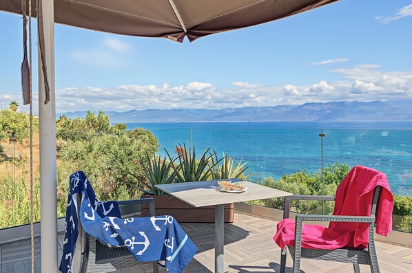 Una terraza con mesa, sillas y vista al mar.