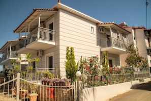 A two-story building with balconies, a gated entrance, and a variety of potted plants and flowers.
