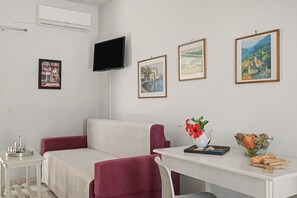Una sala de estar moderna con un sofá blanco, una mesita con un jarrón y fruta, y tres cuadros en la pared.