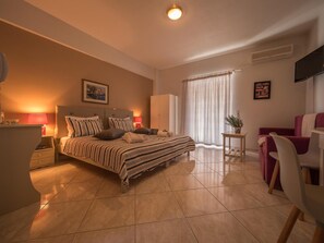 Habitación de hotel con cama, mesitas de noche, escritorio, silla, televisión y ventana con cortinas.