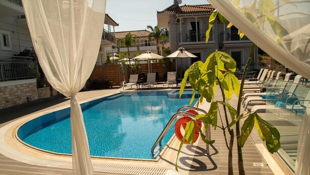 A swimming pool with a clear blue water, surrounded by lounge chairs and umbrellas, with a building in the background.