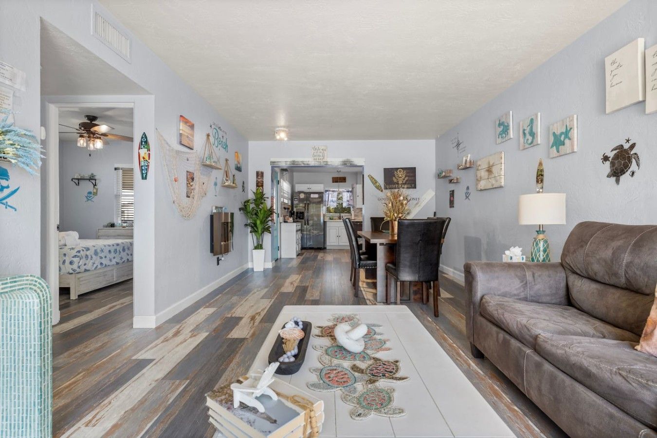 A spacious living room with a brown leather couch, a dining area with a table and chairs, and a kitchen in the background.