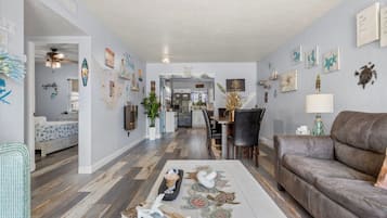 Un vaste salon avec un canapé en cuir marron, un coin repas avec une table et des chaises, et une cuisine à l’arrière-plan.