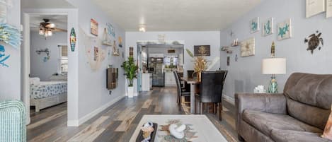 Un vaste salon avec un canapé en cuir marron, un coin repas avec une table et des chaises, et une cuisine à l’arrière-plan.