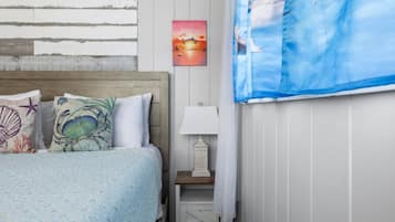Een slaapkamer met een bed, een nachtkastje, een lamp, een schilderij en een raam met gordijnen.