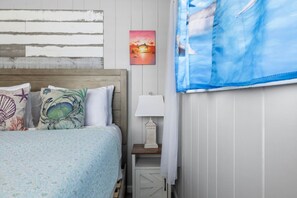 Een slaapkamer met een bed, een nachtkastje, een lamp, een schilderij en een raam met gordijnen.