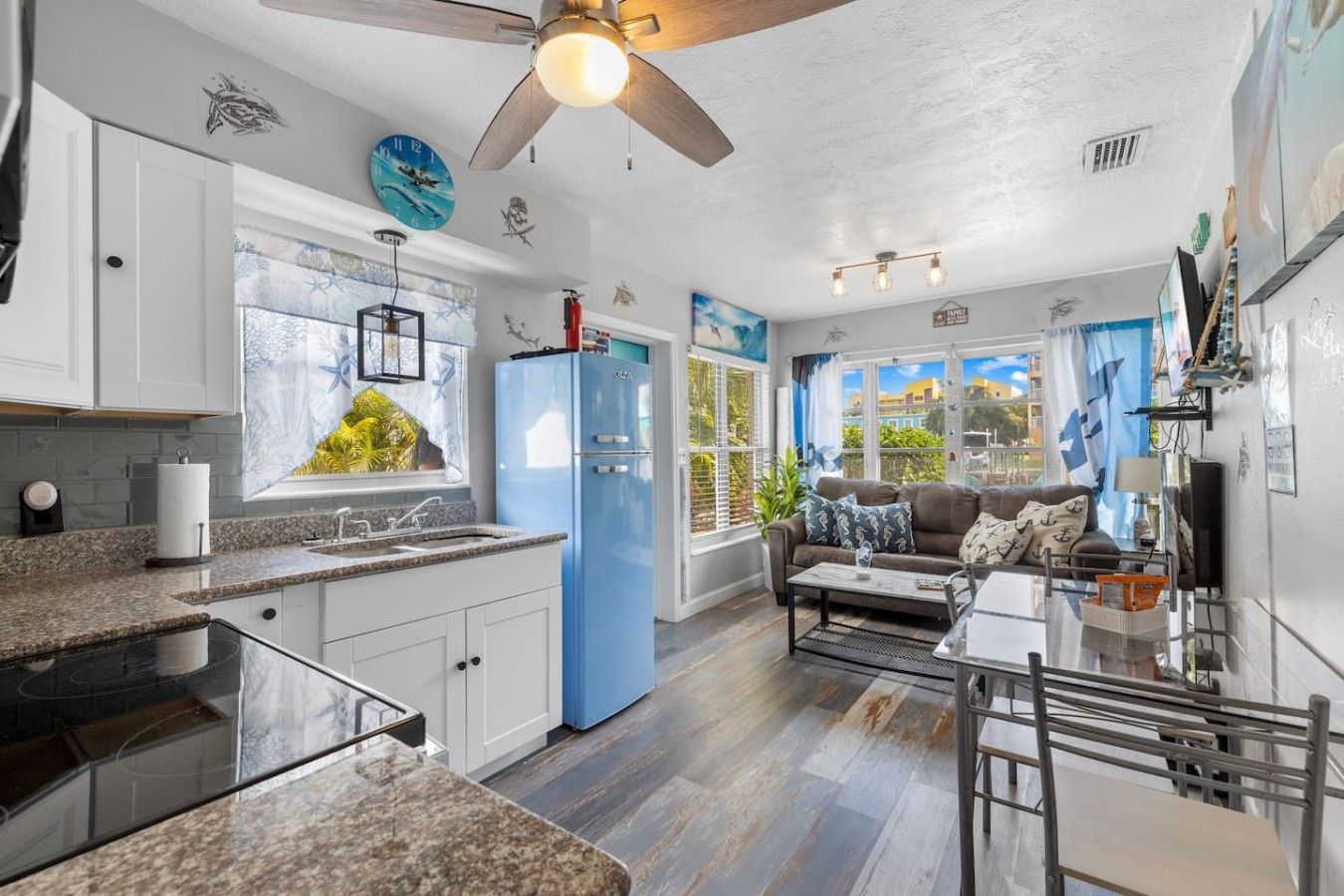 A modern kitchen with a blue refrigerator, a dining area with a glass table, and a ceiling fan.
