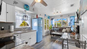 A modern kitchen with a blue refrigerator, a dining area with a glass table, and a ceiling fan.