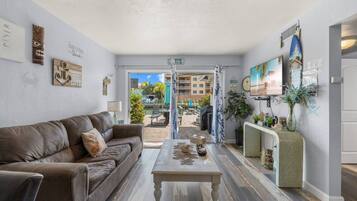 A living room with a brown leather sofa, a coffee table, and a view of an outdoor pool area.