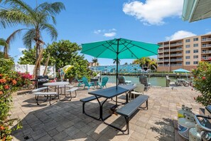Een terras buiten met tafels, stoelen en een grote parasol.