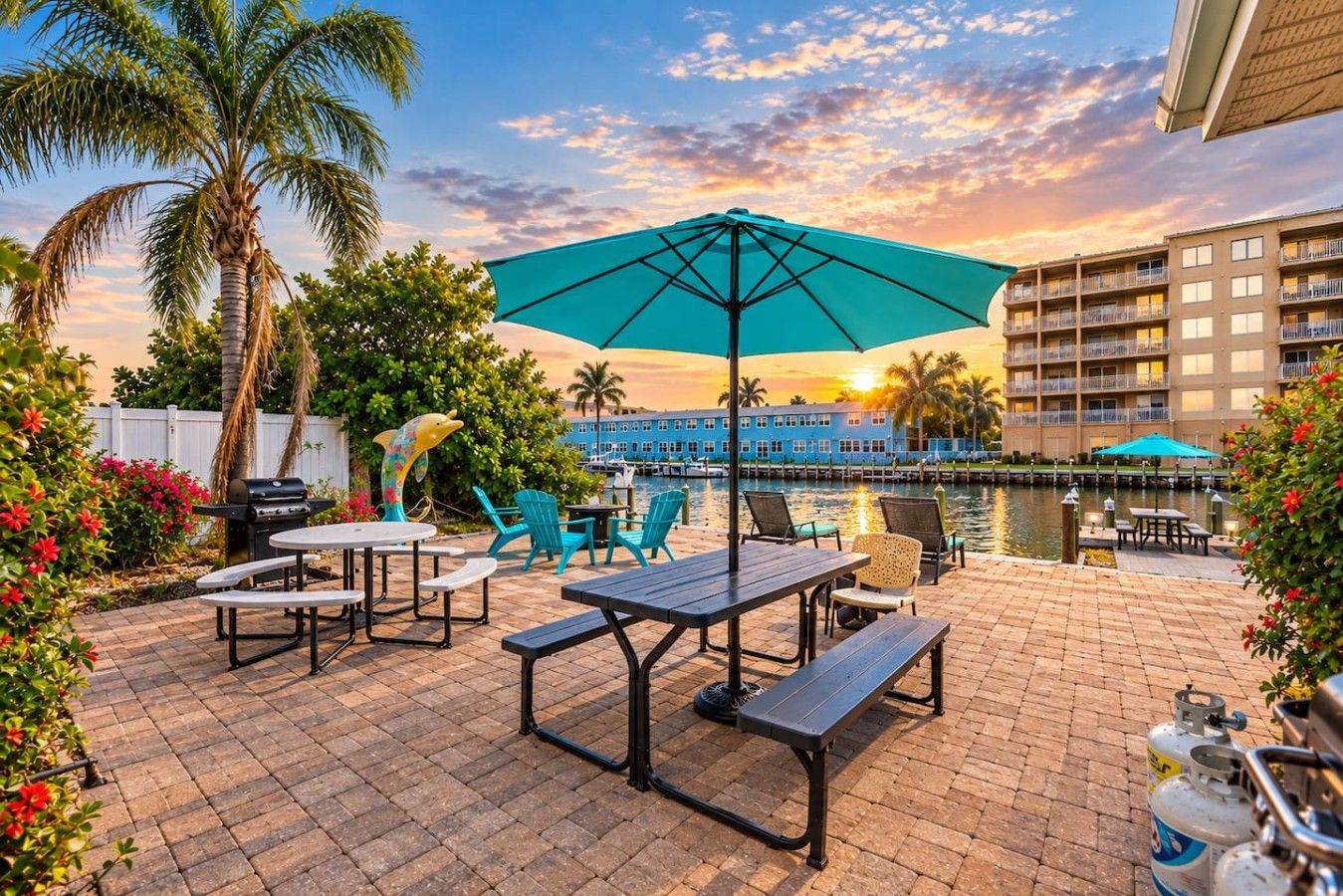 An outdoor patio with tables and chairs, a grill, and a view of a body of water and buildings in the background.