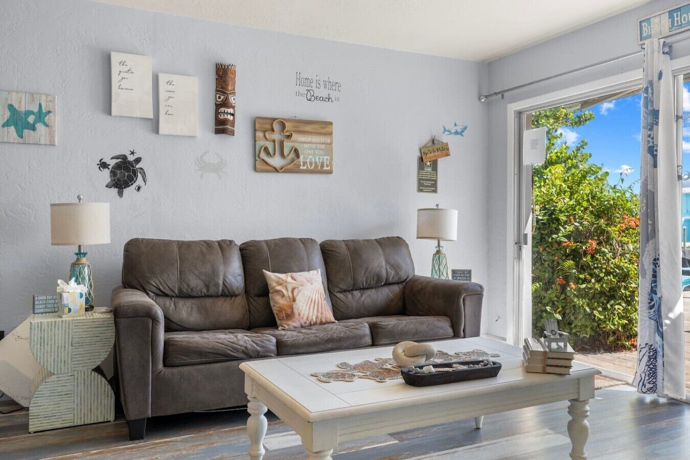 A living room with a brown leather sofa, a white coffee table, and various wall decorations including a turtle and anchor.