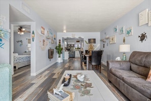 A spacious living room with a brown leather couch, a dining area with a table and chairs, and a kitchen in the background.