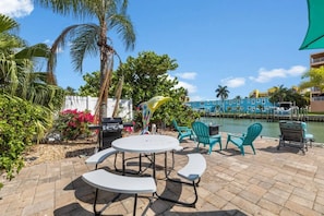 An outdoor patio with a round table and chairs, a grill, and a decorative bird sculpture. - WTR FRONT Home W/Dock | Steps to the Beach! (Treasure Island)