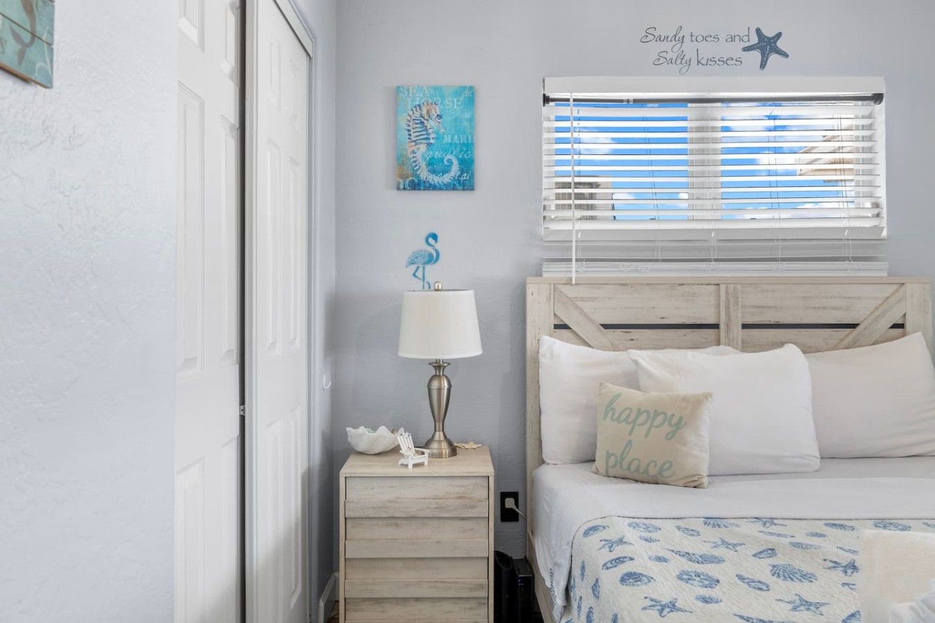 A bedroom with a bed, a nightstand with a lamp, a decorative wall piece, and a window with blinds.