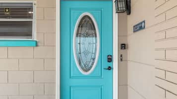 Une porte turquoise avec un panneau en verre, un clavier pour ouvrir la porte et une petite pancarte au-dessus.
