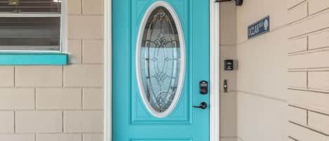 Une porte turquoise avec un panneau en verre, un clavier pour ouvrir la porte et une petite pancarte au-dessus.