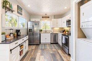 A modern kitchen with white cabinets, stainless steel appliances, and a wooden floor. - Waterfront Home with Dock, Steps to the Beach! (Treasure Island)
