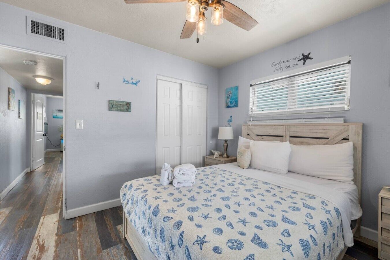 A bedroom with a bed, a ceiling fan, a window with blinds, and a door.