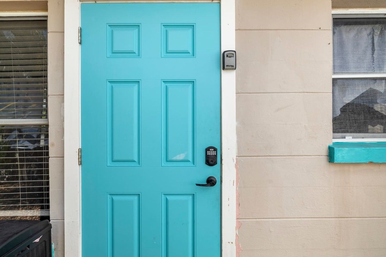 Uma porta azul-turquesa com fechadura digital e uma caixa de correio na parede.