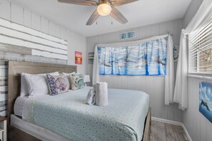 A bedroom with a bed, a ceiling fan, a painting of birds, and a sign that reads 'BEACH HOUSE'. - Cozy WTR Front Home W/ Dock | Steps to the Beach! (Treasure Island)