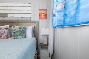 A bedroom with a bed, a nightstand, a lamp, a painting, and a window with curtains. - Cozy WTR Front Home W/ Dock | Steps to the Beach! (Treasure Island)
