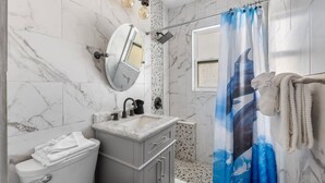 Een badkamer met een marmeren wand, een wastafel met spiegel, een douchegordijn en een handdoekhouder.
