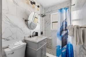 A bathroom with a marble wall, a sink with a mirror, a shower curtain, and a towel rack. - Cozy WTR Front Home W/ Dock | Steps to the Beach! (Treasure Island)