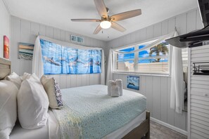 Une chambre avec un lit, un ventilateur de plafond, une fenêtre donnant sur un beau paysage et une pancarte sur laquelle on peut lire « MAISON DE PLAGE ».