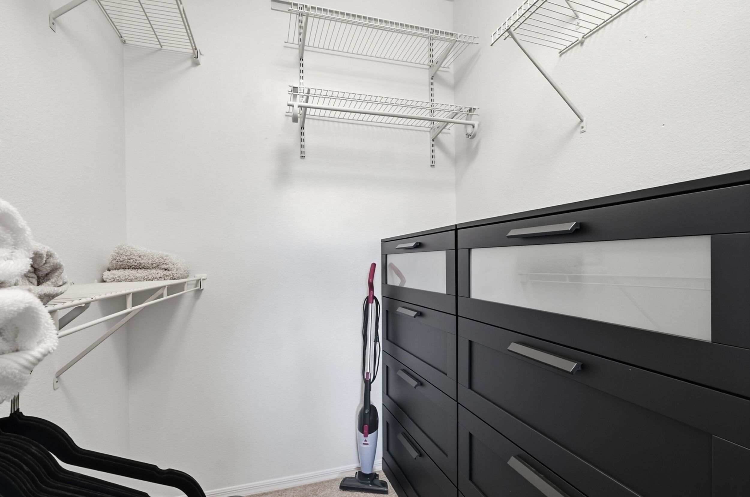 Un placard avec une commode noire et des étagères en fil de métal.