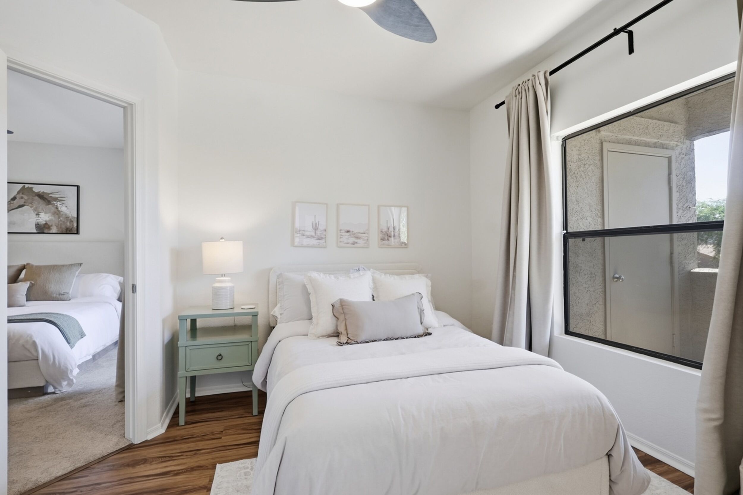 A bedroom with a bed, nightstands, a window with curtains, and artwork on the wall.